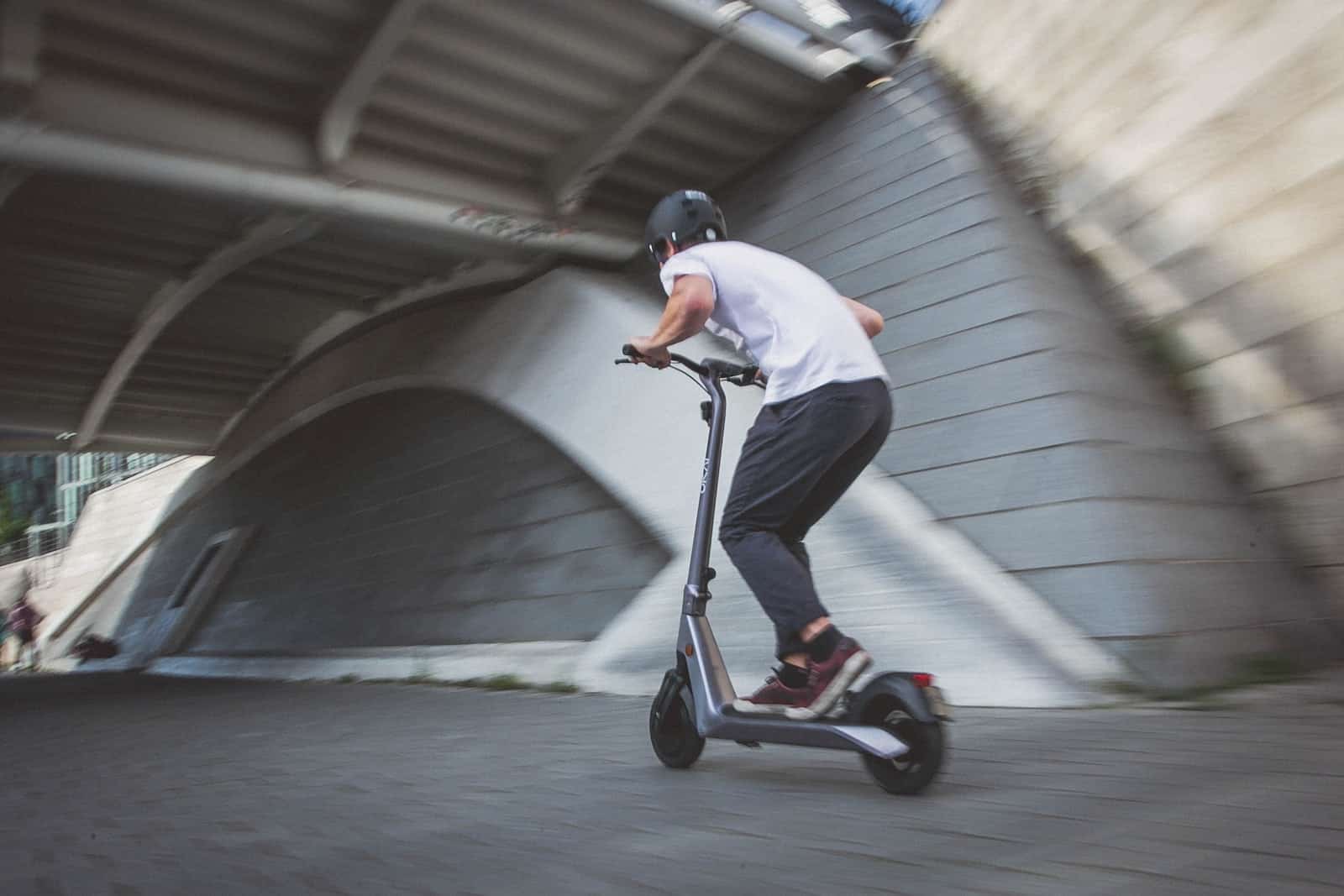 man in white t-shirt riding black and red kick scooter on gray concrete road during