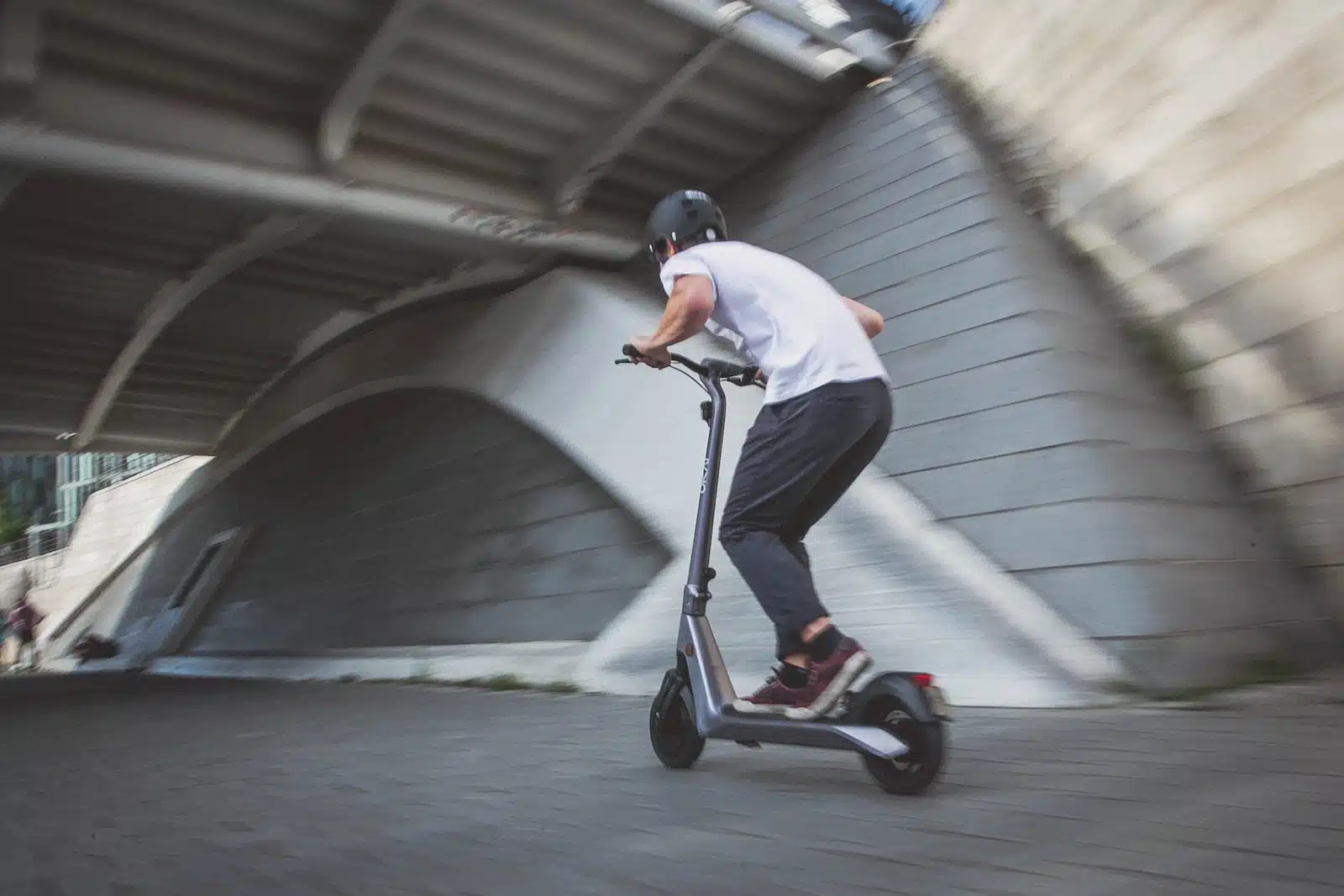 man in white t-shirt riding black and red kick scooter on gray concrete road during